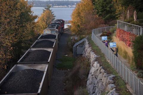 Two protesters holding signs as a train loaded with coal passes. Photo by Paul K. Anderson. Two protesters holding signs as a train loaded with coal passes. Photo by Paul K. Anderson.